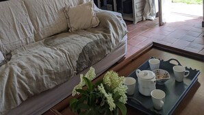 A cozy room with a sofa, a table with cups and a teapot, a lamp, a painting, and a view of greenery outside. - Romantic french cottage 6 persons with pool, 15 min from Rocamadour/Dordogne (Reilhaguet)