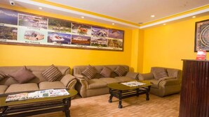 Una habitación con una pared amarilla, un sofá marrón, una mesa de centro de madera y un tablón de anuncios con carteles de viajes.