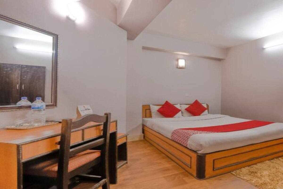 A bedroom with a bed, a desk, a chair, a wardrobe, and a mirror.