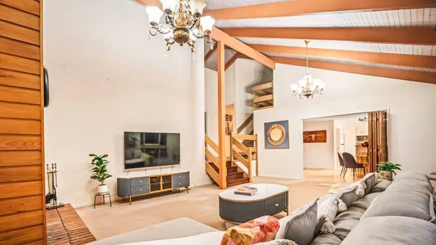 Una sala de estar moderna con un sofá grande, un televisor y una escalera que sube a un nivel superior.