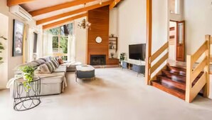 Un salón amplio con chimenea, un conjunto de sofás, un televisor y una escalera.