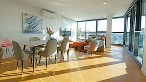 Ampla sala de estar com mesa de jantar, cadeiras, sofá e uma grande janela com vista.