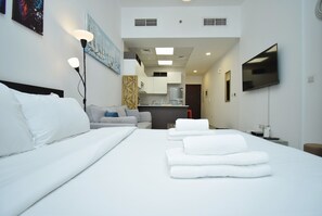 A hotel room with a large bed, a desk, a flat-screen TV, and a kitchenette.