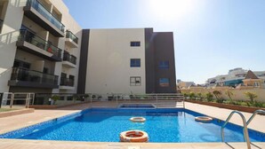 A modern building with a rooftop swimming pool, featuring a clear sky and a view of neighboring buildings. - JVC studio Joya Verde with terrace - 360 vacation (Dubai)