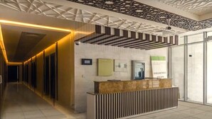 A hotel reception area with a modern design, featuring a reception desk, a patterned ceiling, and a sign advertising show apartments. - JVC studio Joya Verde with terrace - 360 vacation (Dubai)