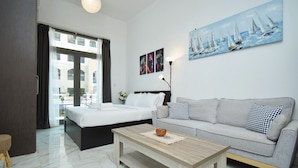 A modern hotel room with a bed, a sofa, a coffee table, and a painting of sailboats on the wall. - JVC studio Joya Verde with terrace - 360 vacation (Dubai)