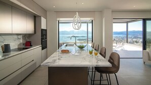 Una cucina moderna con un piano di lavoro in marmo, un'isola centrale con posti a sedere e vista sulla città e sulle montagne attraverso ampie finestre.