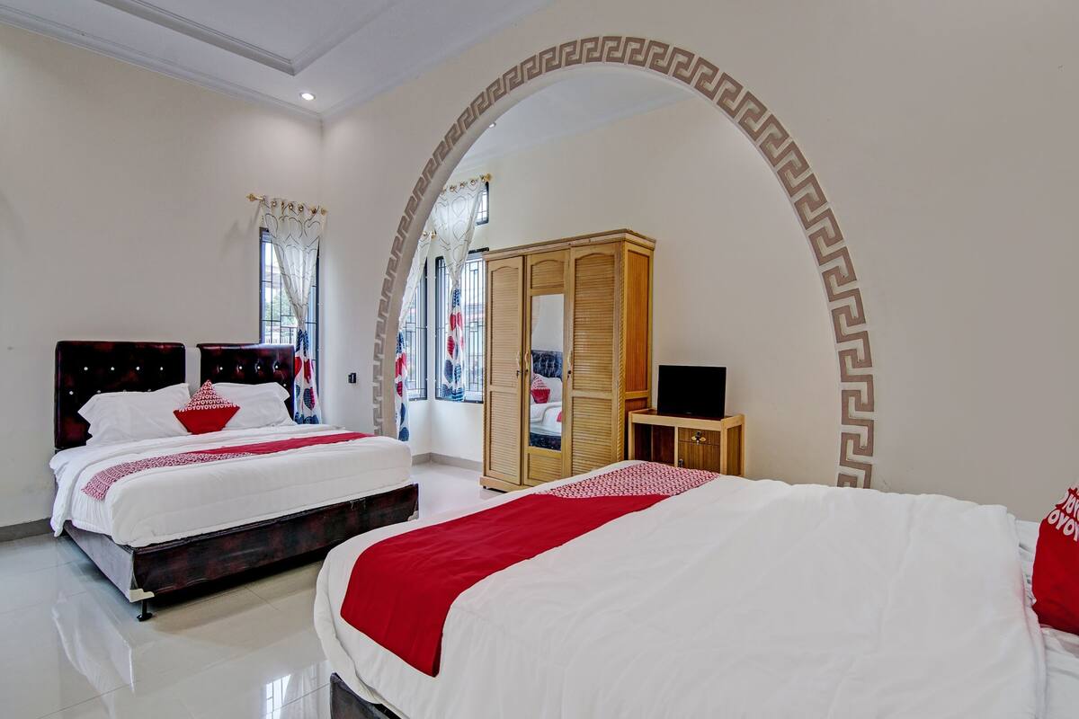 A hotel room with two beds, a wardrobe, a television, and a decorative archway.