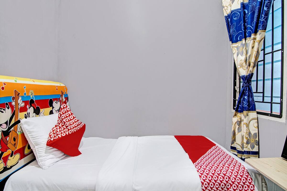 A bed with white and red bedding, a Mickey Mouse themed headboard, and a window with blue curtains.