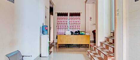 A hotel reception area with a reception desk, a water dispenser, a bench, and a staircase.