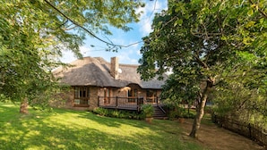 Een huis met rieten dak, omgeven door weelderige begroeiing en een houten omheining.