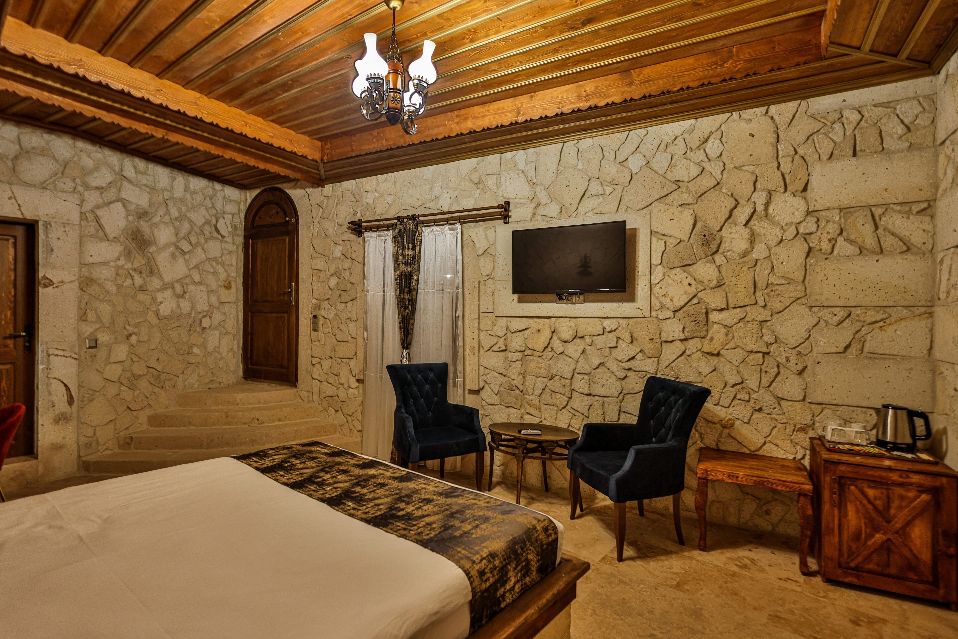 Un dormitorio con pared de piedra, una cama, dos sillas, una mesita, un televisor y un armario de madera.