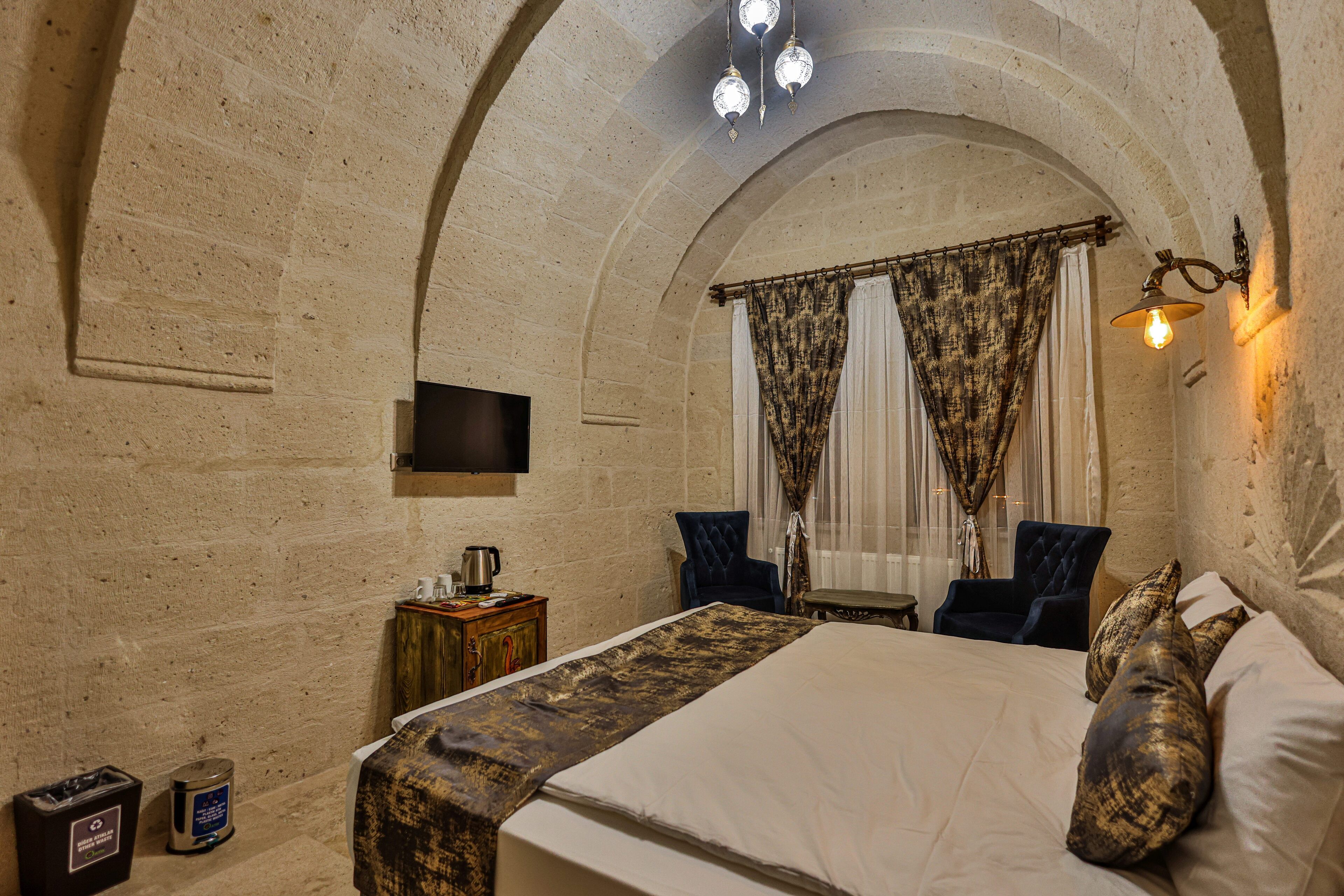 A bedroom with a large bed, two armchairs, a small table, a TV, and a chandelier.