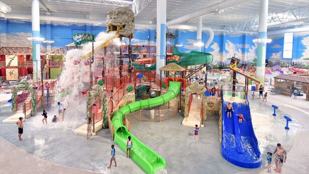 Ein Indoor-Wasserpark mit mehreren Rutschen und Wasserspielen, darunter eine große, grüne Rutsche und eine blaue Rutsche.
