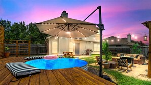 Ein Garten mit Schwimmbad, Holzterrasse, Gartenmöbeln und Lichterketten.