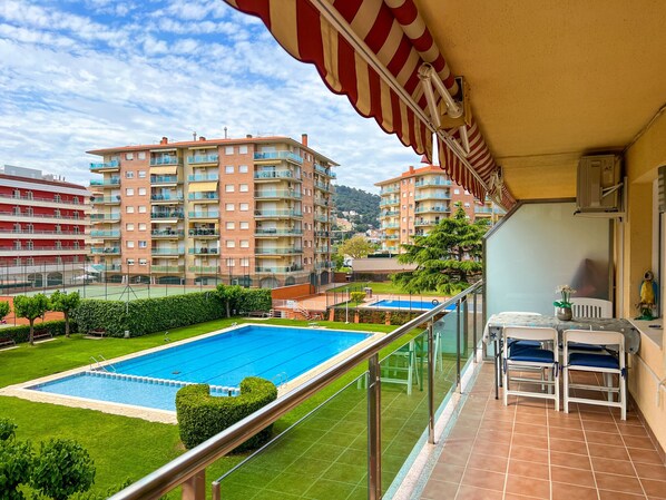 Uma varanda com piscina, vista para prédios de apartamentos e um terraço com mesa e cadeiras.