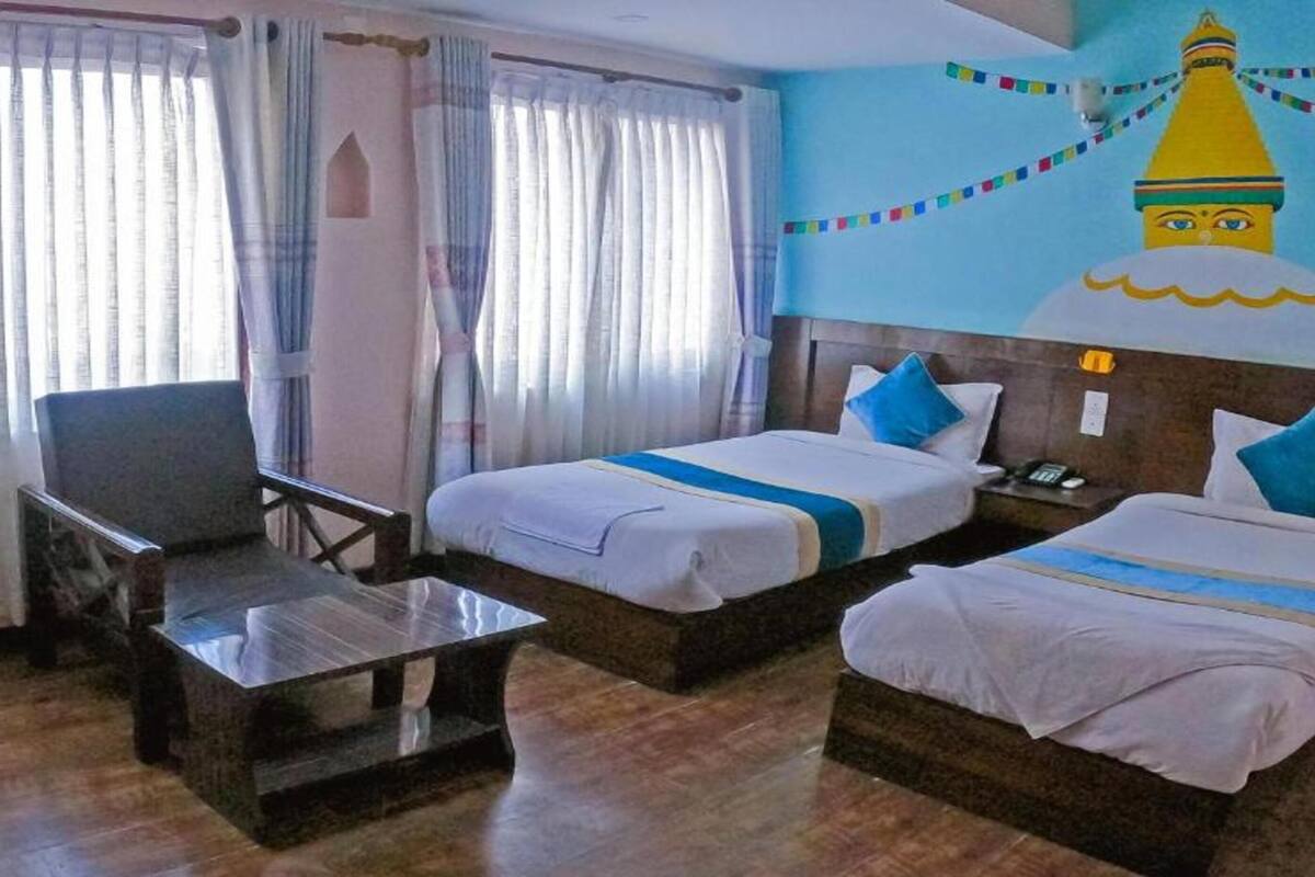 Habitación de hotel con dos camas individuales, un televisor, una mesa de centro de madera y un mural de una montaña en la pared.