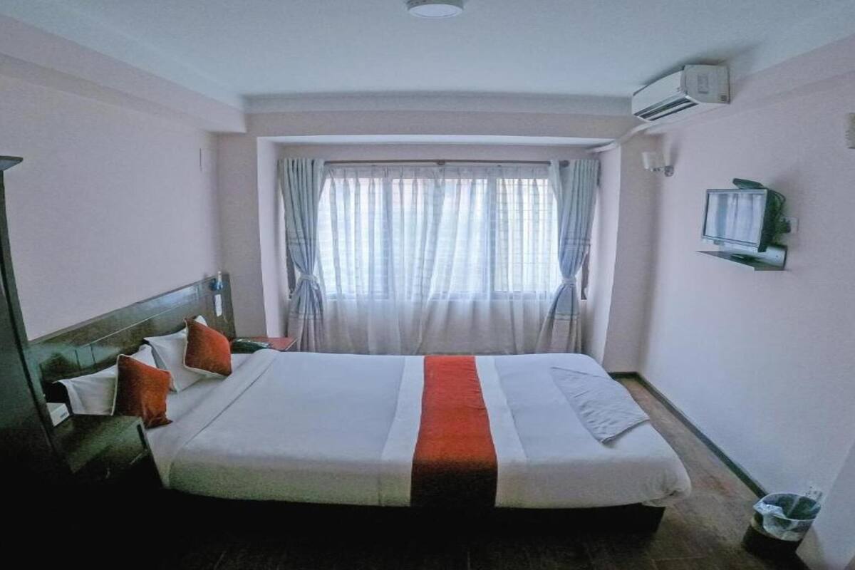 Una habitación de hotel con cama, armario, ventana con cortinas, aire acondicionado y televisión.