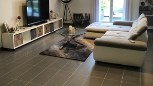 A modern living room with a flat-screen TV, a glass-top coffee table, a sofa, and a floor lamp. - Grande Villa Avec Piscine Proche mer + Bateau (Mireval)