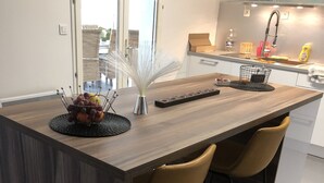 A modern kitchen with a central island, two bar stools, and a large window. - Grande Villa Avec Piscine Proche mer + Bateau (Mireval)