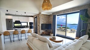 Een moderne woonkamer met een grote bank, een televisie en een eethoek met rieten stoelen.