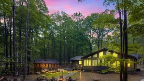 Une cabane dotée d’une terrasse et d’un foyer, entourée de grands arbres et surplombant un ciel dégagé.