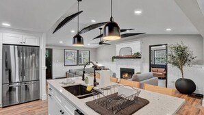 Une cuisine moderne dotée d’un réfrigérateur en acier inoxydable, d’un grand îlot central avec un évier, de luminaires suspendus et d’un ventilateur de plafond.