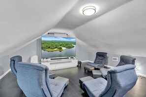 Relax in this stylish attic room with a large flat-screen TV, grey armchairs, and a dark-toned ottoman.