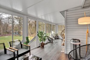 Relax on the covered porch with a view of the surrounding landscape, featuring a bench and lounge chairs.