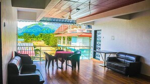 Una habitación con suelo de madera, una mesa roja con sillas, un sofá de cuero negro y vistas a una montaña y edificios.