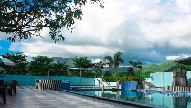 Piscina con solárium empedrado, zona de estar techada y vistas a montañas y vegetación.