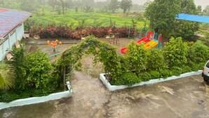 Un parque infantil con toboganes y columpios, rodeado de vegetación y un edificio de techo rojo.
