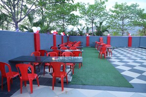 An outdoor seating area with red chairs and tables, surrounded by a blue wall and trees. - Wayfare SP Resort (Panvel)