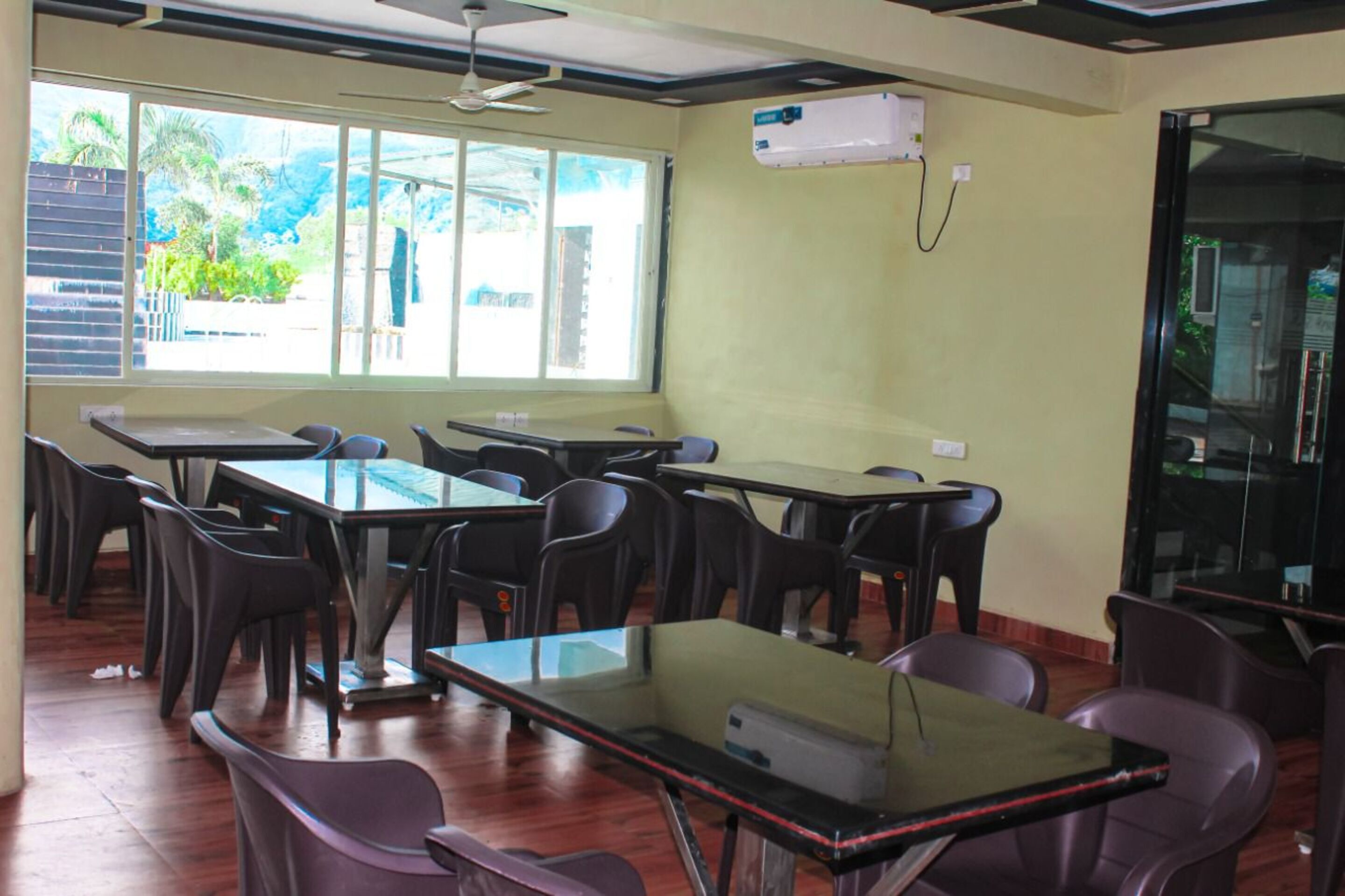 A classroom with tables and chairs, a ceiling fan, and a window with a view of greenery.