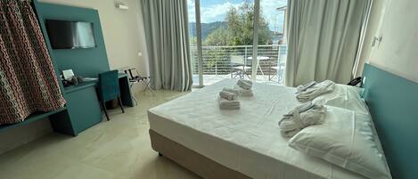 Habitación de hotel con una cama grande, un escritorio, un televisor y un balcón con vistas al exterior.