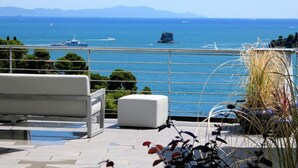 Une terrasse avec vue sur la mer, un banc blanc et des plantes en pot.