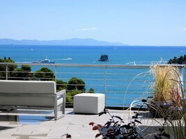 Una terraza con vistas al mar, un banco blanco y plantas en macetas.