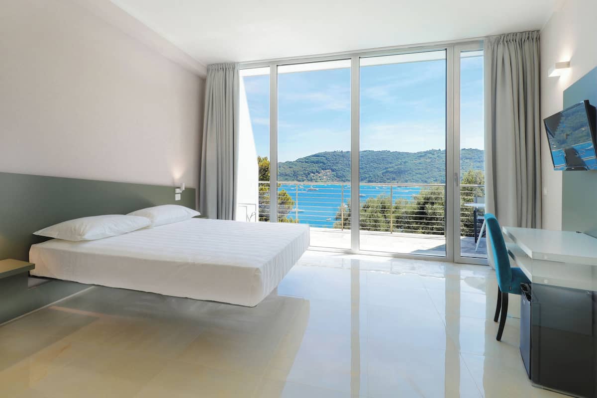 A modern hotel room with a large bed, a desk, and a view of the sea.