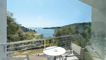 A balcony with a white table and chairs, overlooking a coastal landscape with trees and boats.