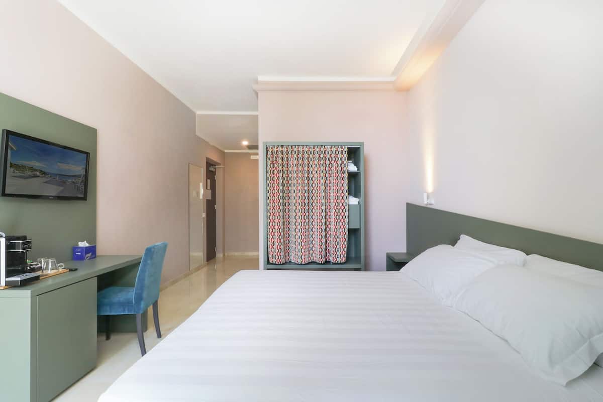 A hotel room with a bed, a desk, a chair, a television, and a patterned curtain.