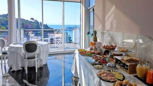 Une table de buffet proposant divers plats et offrant une vue sur la mer grâce à de grandes fenêtres.