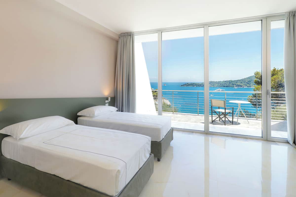 A hotel room with two beds, a balcony with a table and chairs, and a view of the sea.