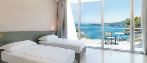 A hotel room with two beds, a balcony with a table and chairs, and a view of the sea.