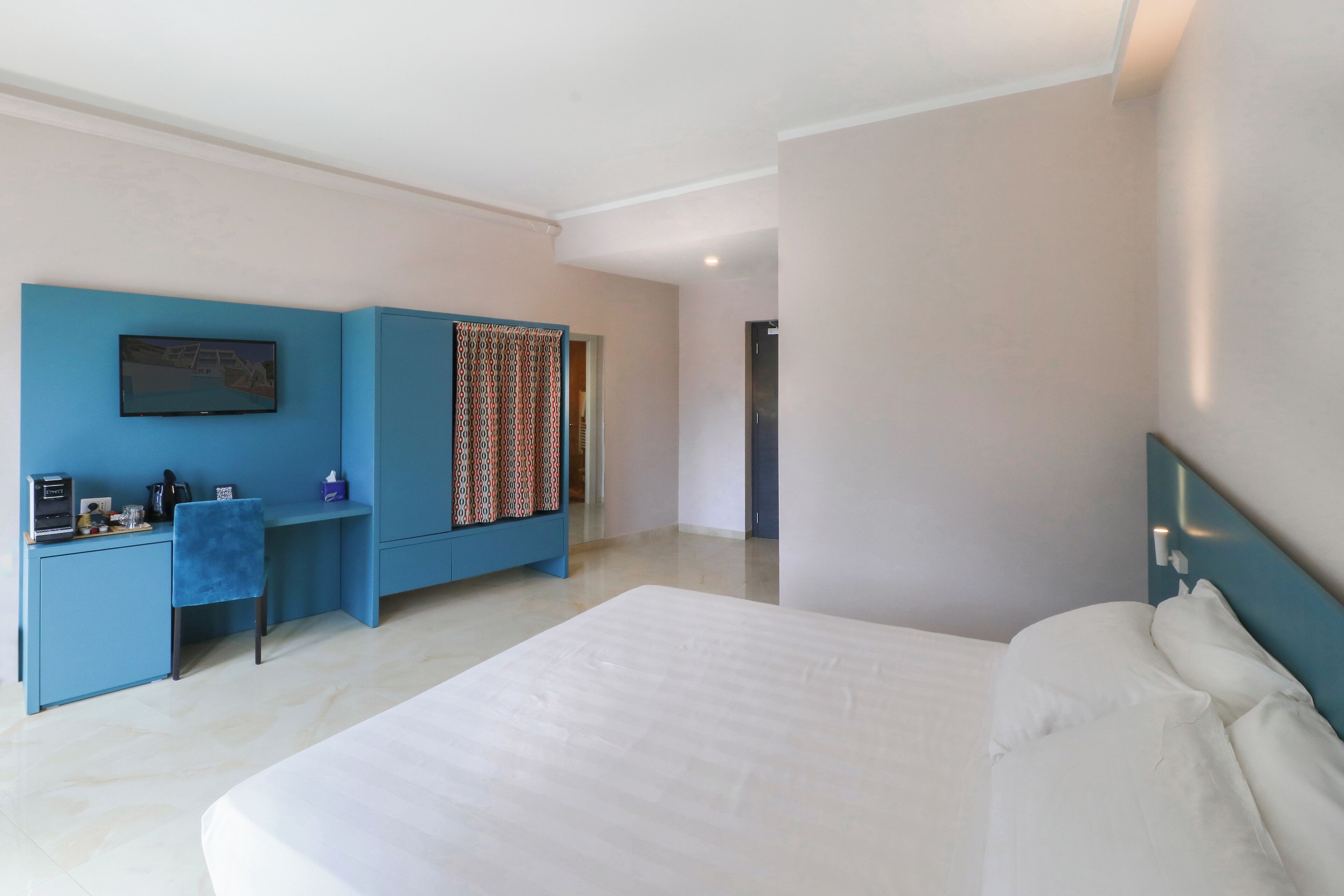 Una habitación de hotel con una cama grande, un escritorio con silla, un televisor y una cortina estampada.