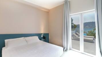 Een hotelkamer met een groot bed, een nachtkastje, een telefoon en uitzicht op een balkon met buitenmeubilair.