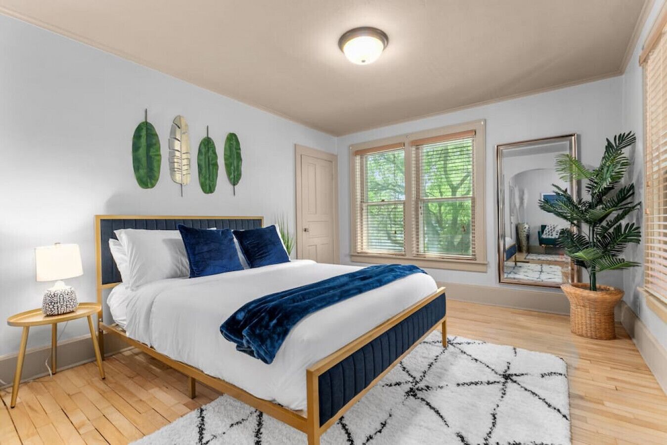 Quarto com cama, mesa de cabeceira, abajur e uma janela grande com persianas.