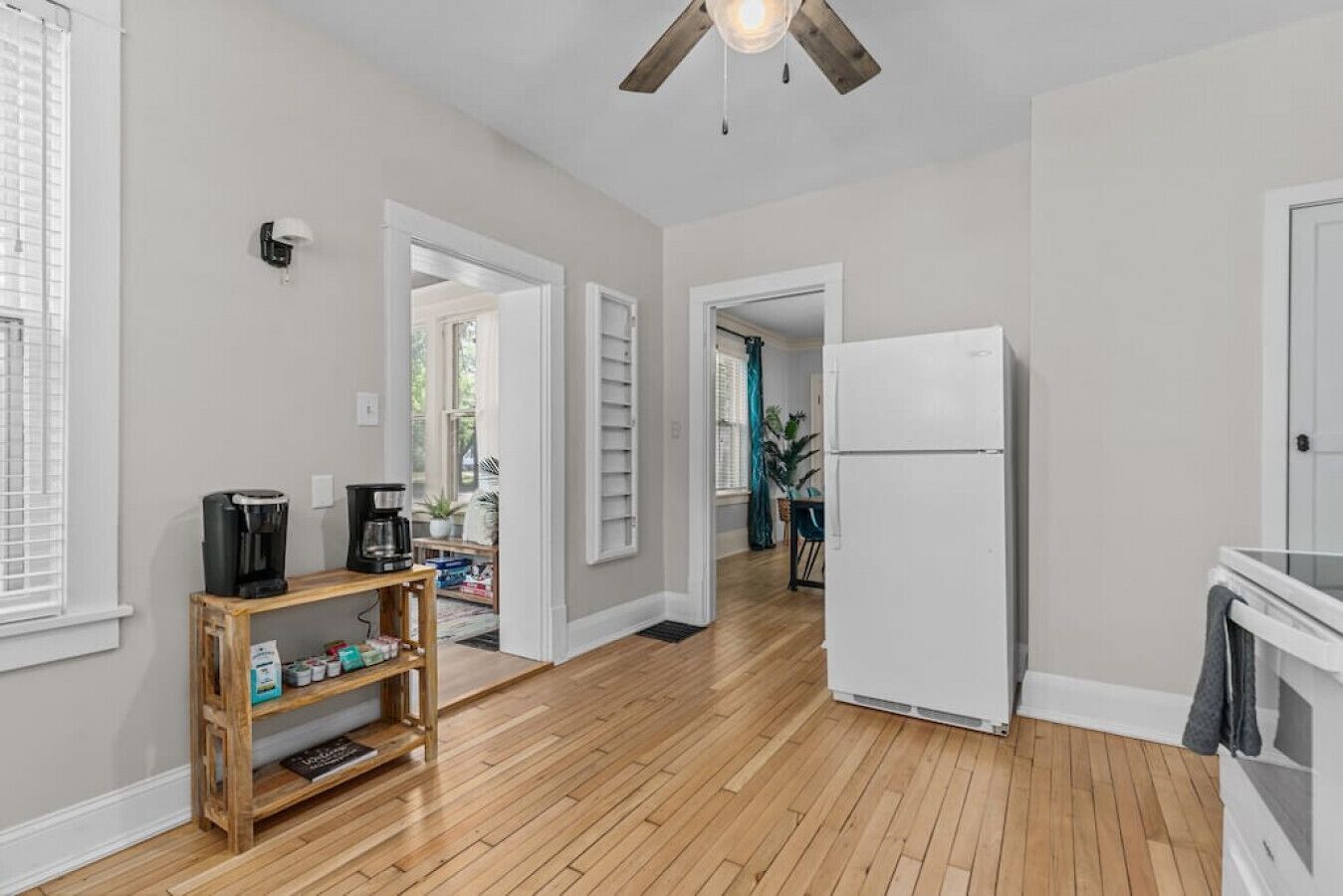 Una cocina amplia con suelo de madera, un refrigerador blanco y una cafetera sobre una estantería de madera.