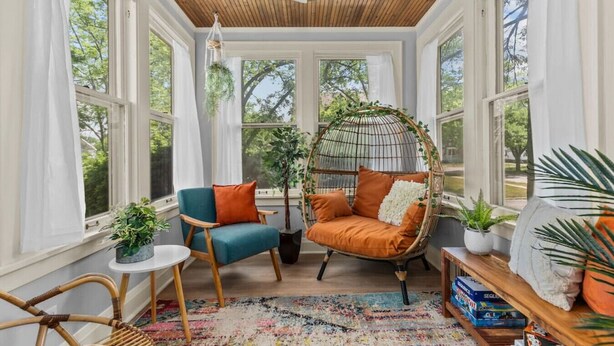 Un solarium con una silla colgante, una silla azul y una mesita con plantas.