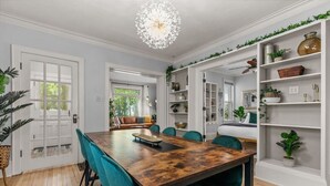 Un comedor con una mesa de madera y sillas color turquesa, una lámpara de araña, y estantes con plantas y objetos decorativos.