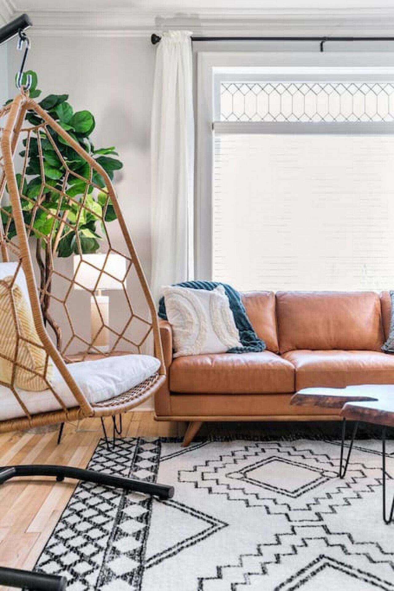 Una sala de estar con un sofá de cuero marrón, una silla colgante, una planta grande y un tapiz estampado.